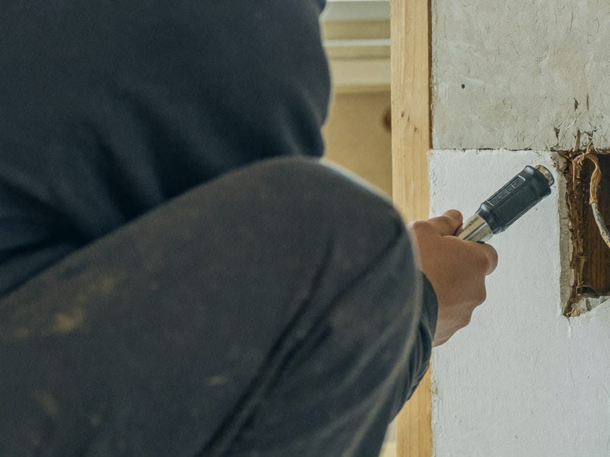A tradesperson crouched at a stripped-back wall, shining a torch on old perished cable pulled out of the plaster.